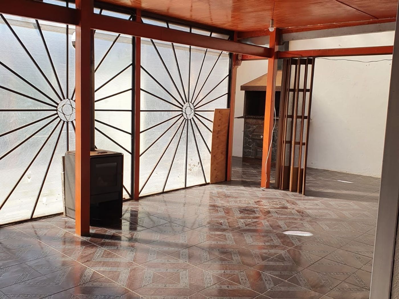 Terraza techada con vigas de madera a la vista, piso cerámico y reja ornamental divisoria.