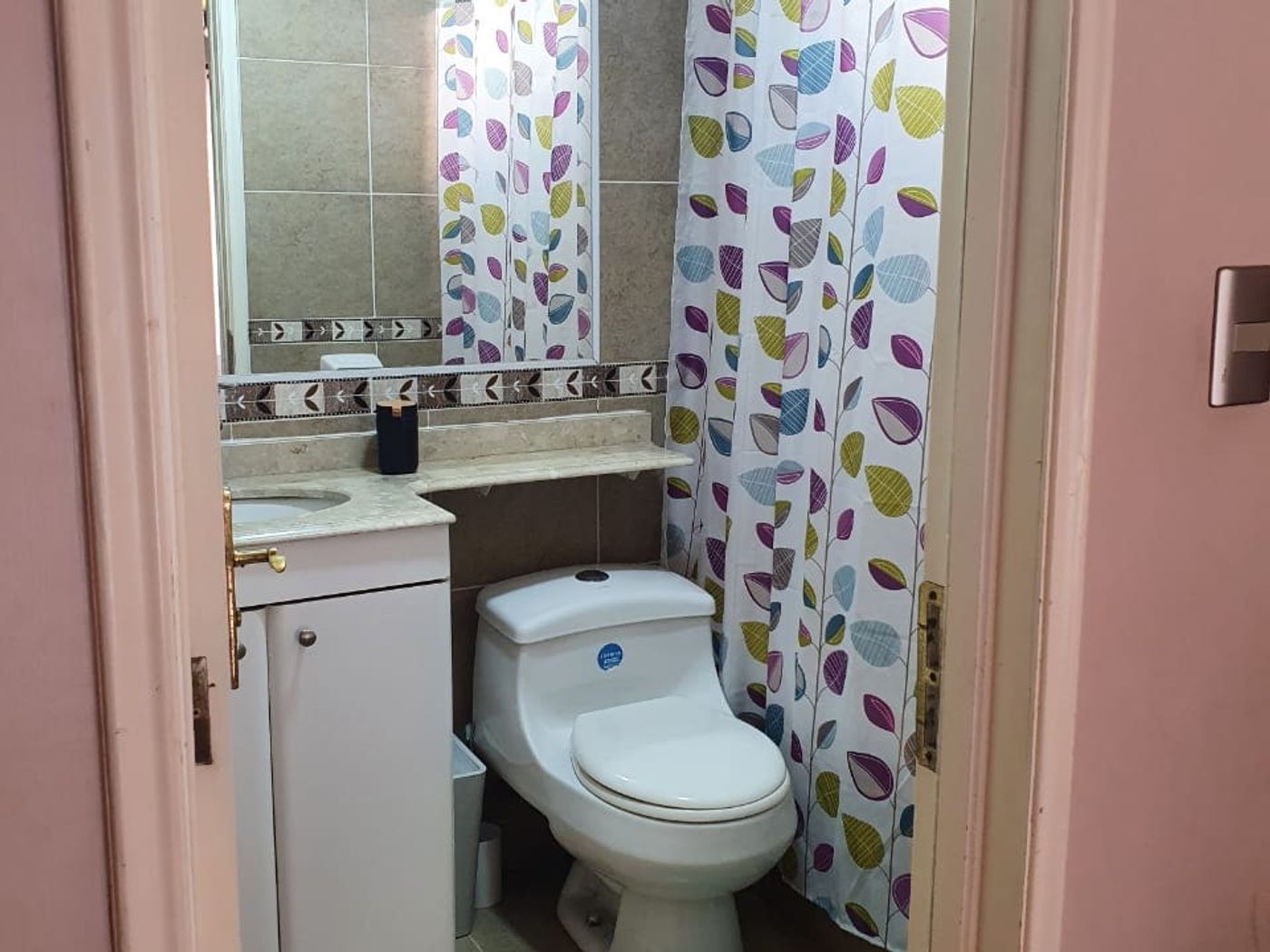 Baño con inodoro, cortina de ducha estampada con hojas y alfombra turquesa en el piso.