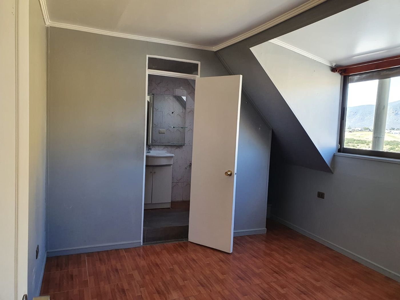 Dormitorio en segundo piso abuhardillado con cielo de madera, piso flotante y acceso a baño privado.