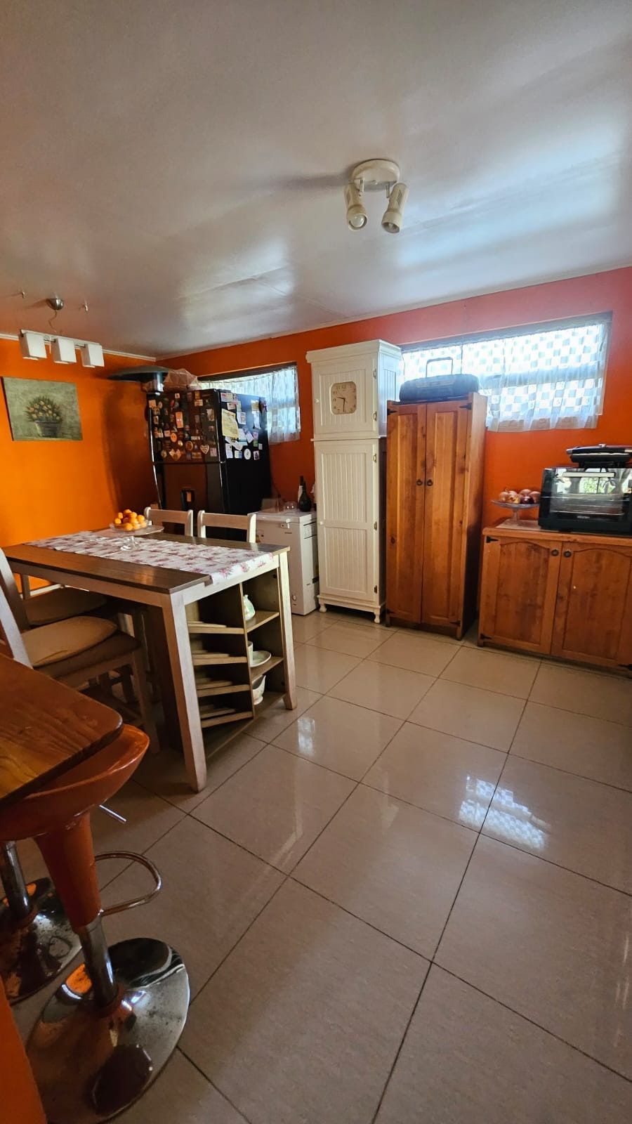 Cocina comedor de muros naranjos, con mesa y sillas, refrigerador y mueble bar al fondo.