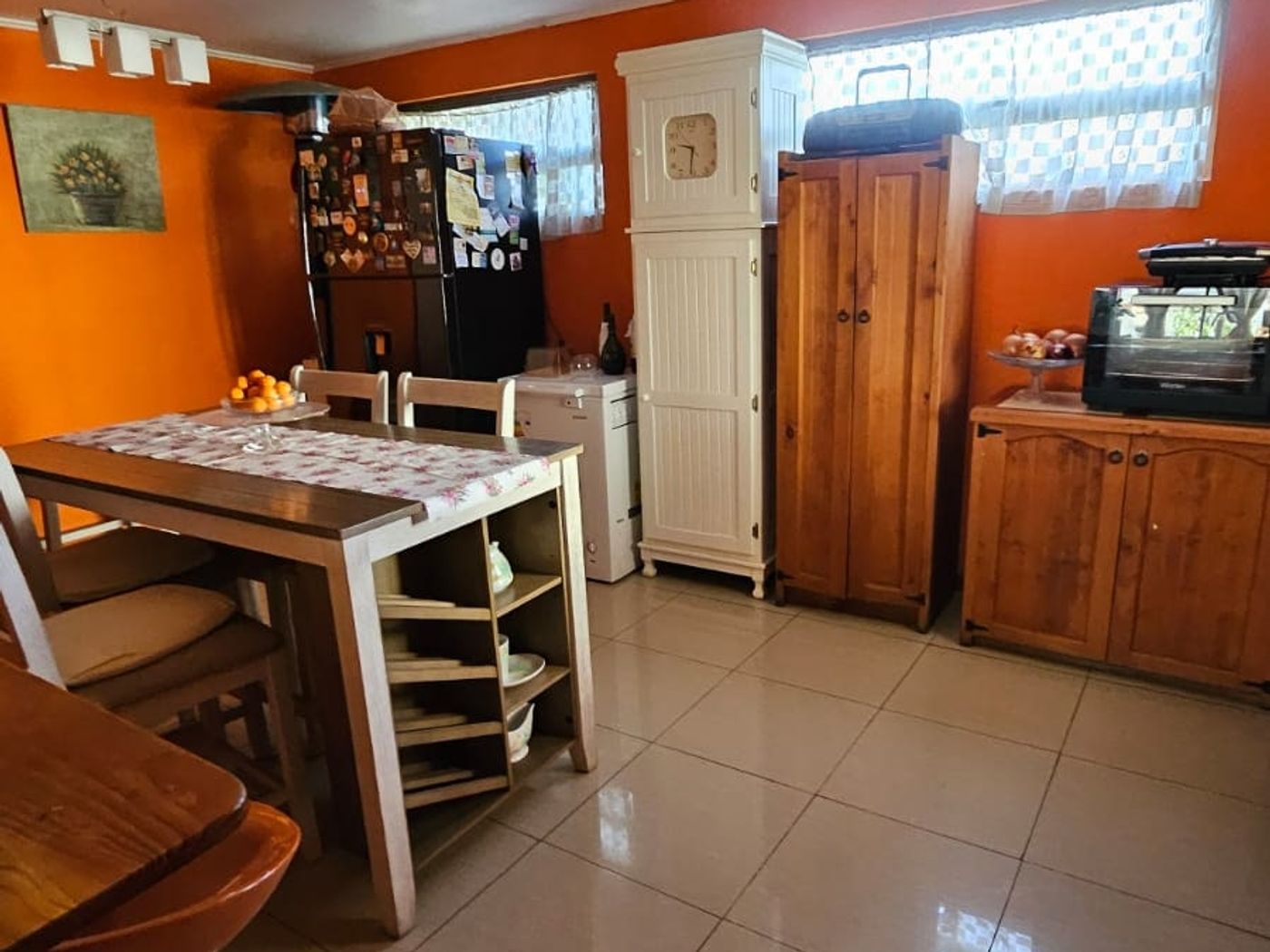 Cocina comedor de muros naranjos, con mesa y sillas, refrigerador y mueble bar al fondo.