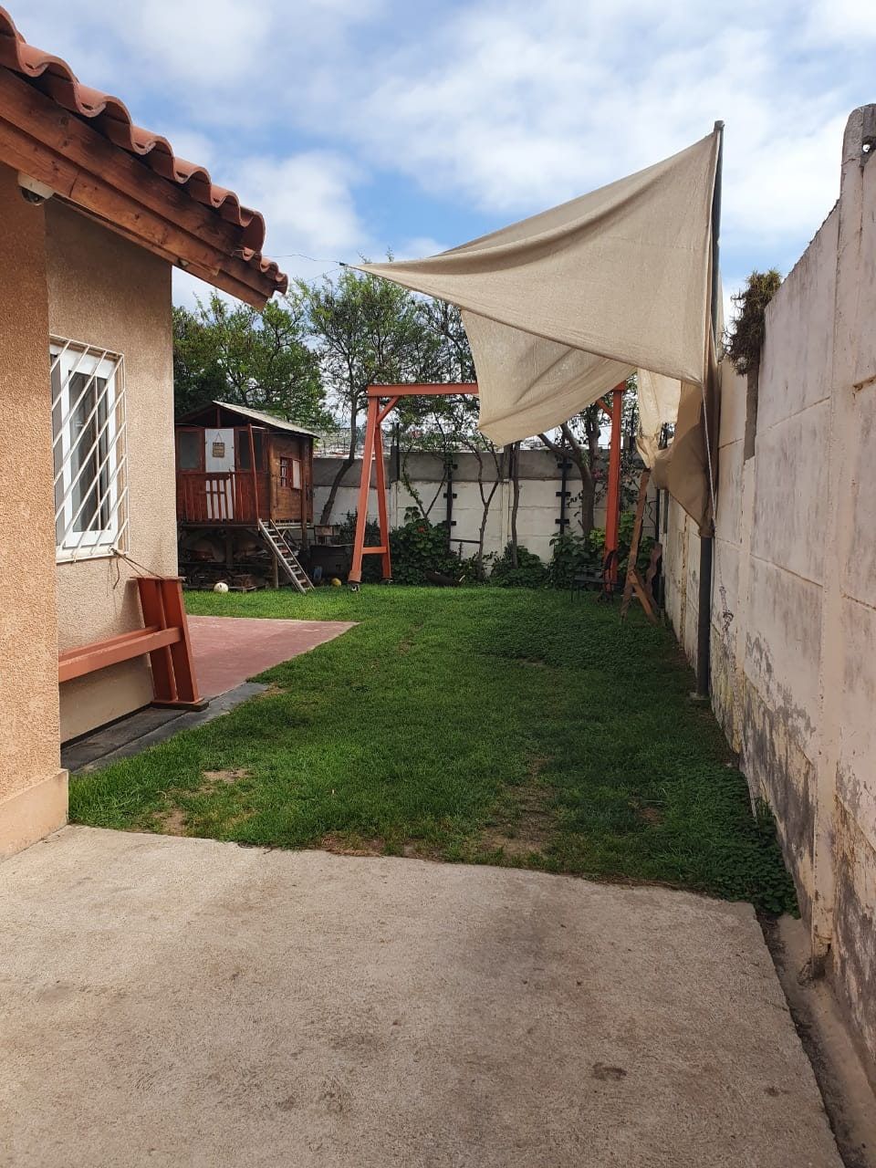 Patio trasero con pasto, quincho de madera y toldo triangular sobre estructura de fierro.
