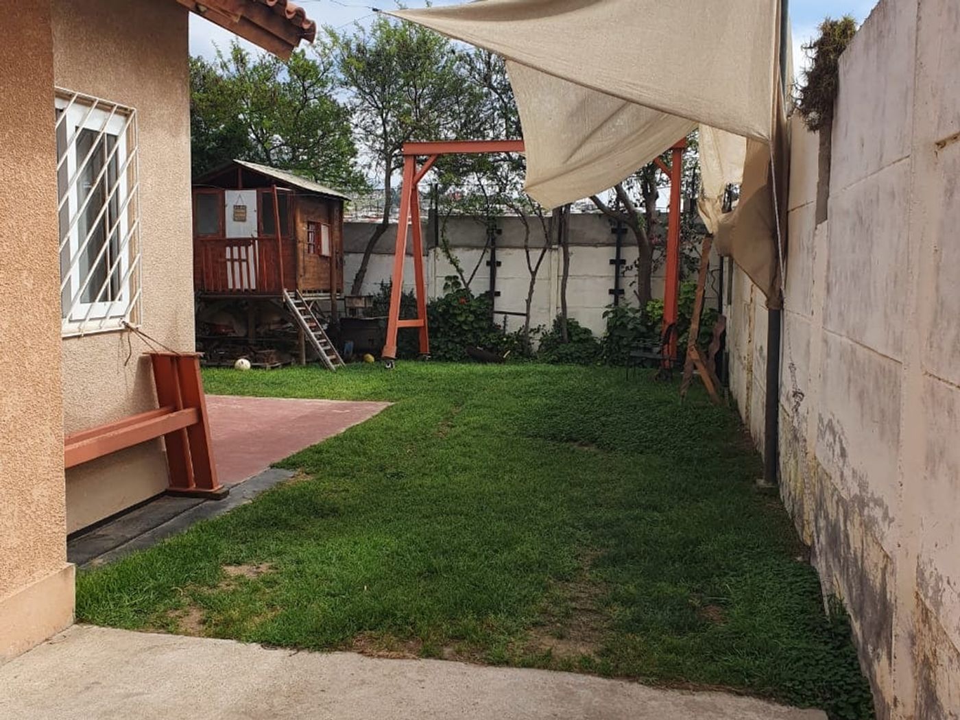 Patio trasero con pasto, quincho de madera y toldo triangular sobre estructura de fierro.