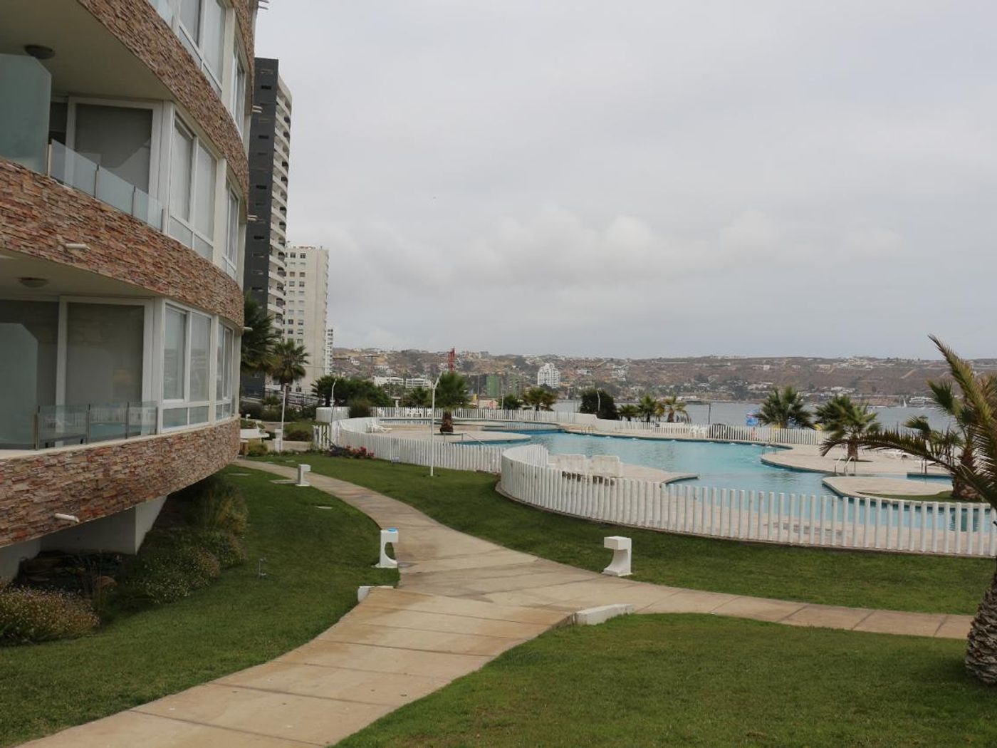 Fachada del edificio con balcones curvos en piedra pizarra, áreas verdes y piscina exterior.