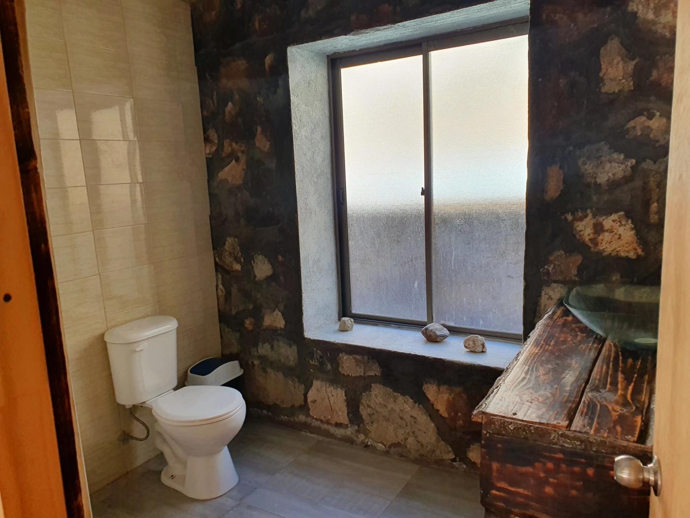 Baño de piedra con WC, ventana esmerilada y mueble antiguo