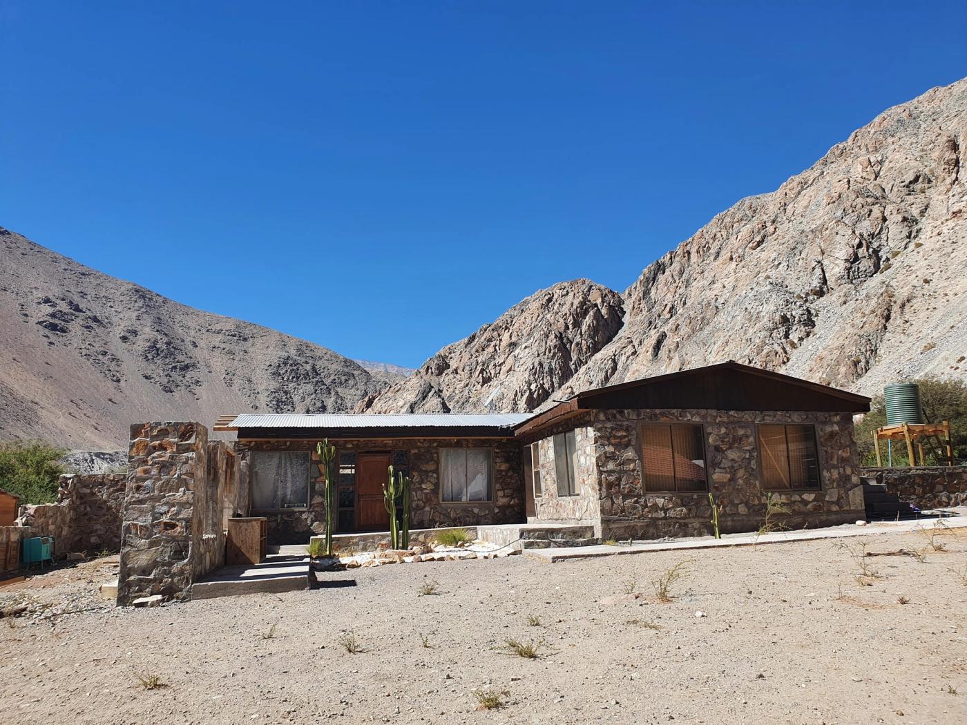 Casa de piedra con cactus y estanque verde al costado