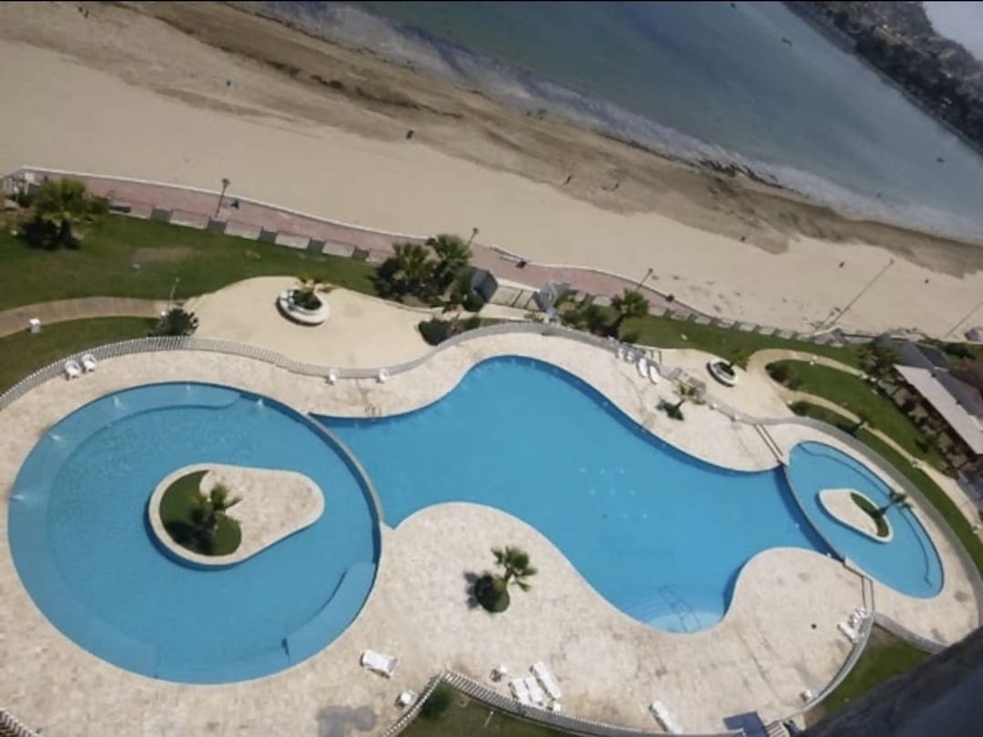 Vista en altura hacia la piscina, jardines y áreas comunes del condominio desde el departamento.