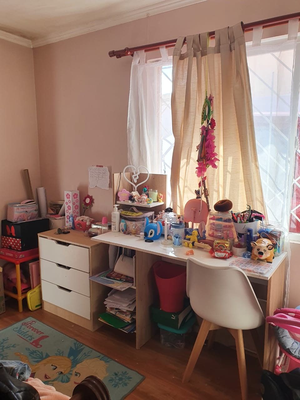 Dormitorio infantil con escritorio, repisas y alfombra, con la superficie cubierta de útiles y juguetes.