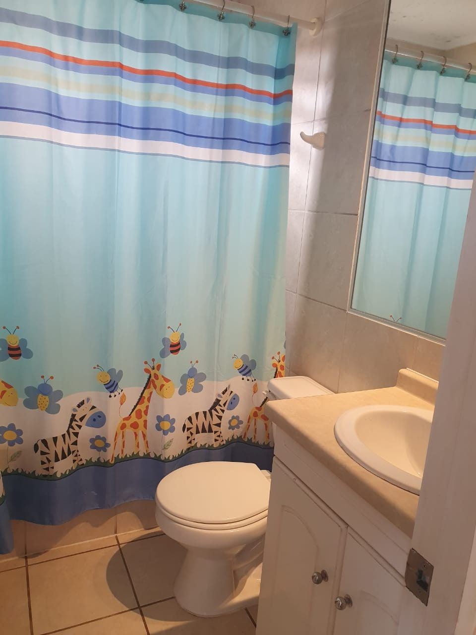 Baño con inodoro, lavamanos y cortina de baño infantil con jirafas y cebras.