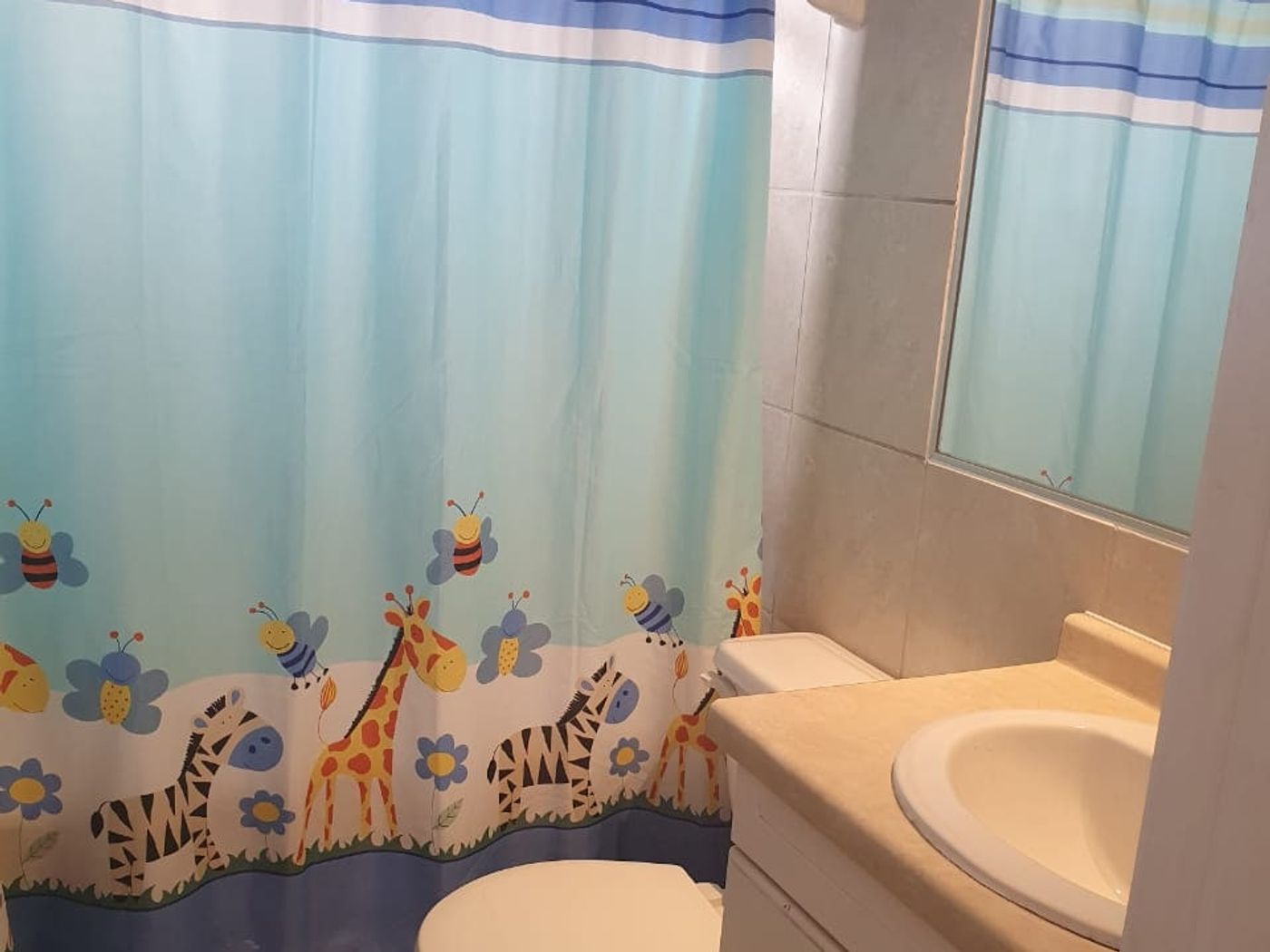 Baño con inodoro, lavamanos y cortina de baño infantil con jirafas y cebras.