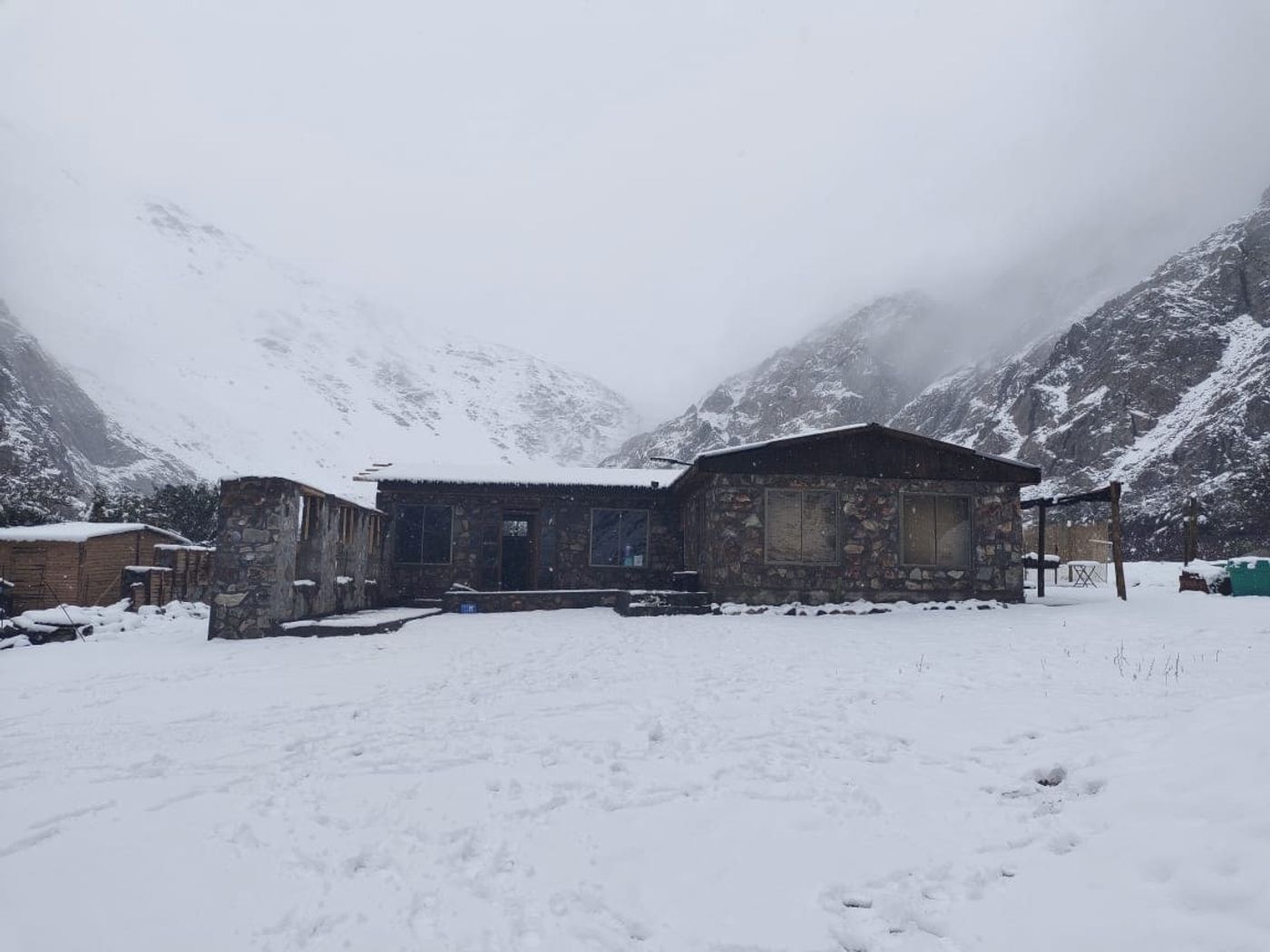 Casa de piedra cubierta de nieve entre cerros nublados