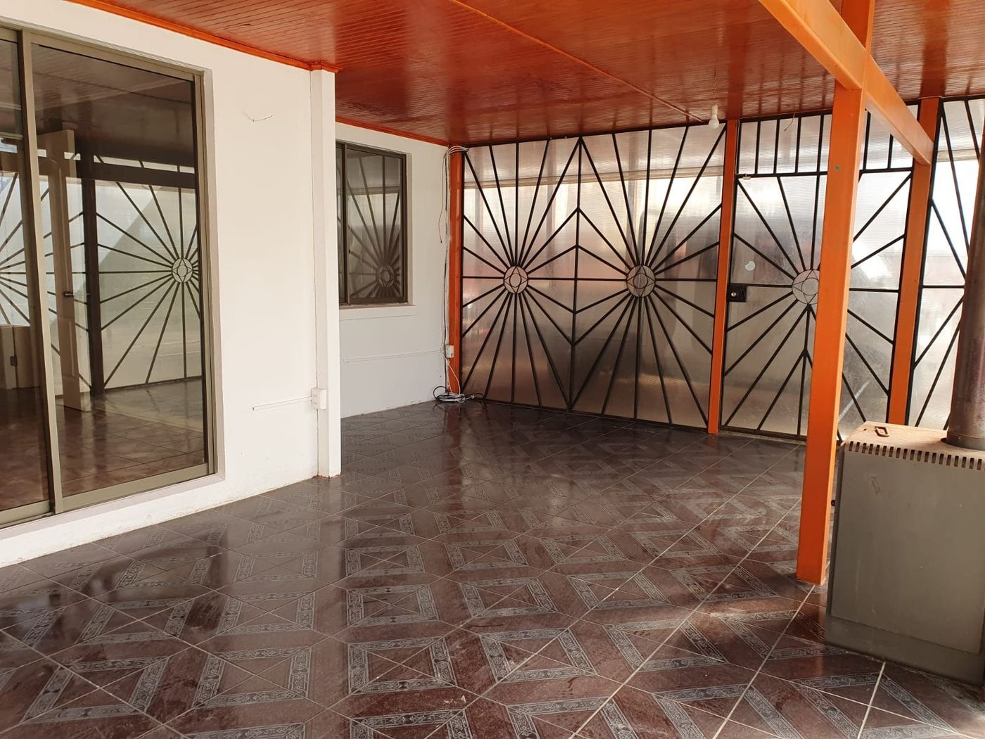 Amplia terraza interior techada con vigas de madera, cerámica brillante y mamparas acristaladas.
