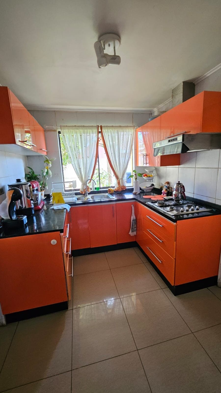 Cocina equipada con muebles naranjos, cocina a gas, campana extractora y ventana con cortinas.