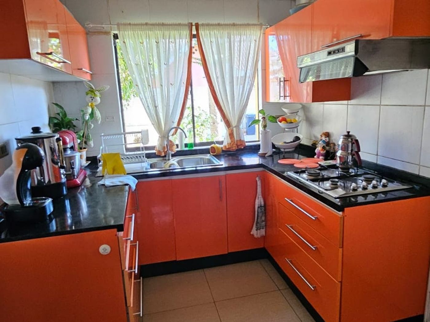Cocina equipada con muebles naranjos, cocina a gas, campana extractora y ventana con cortinas.