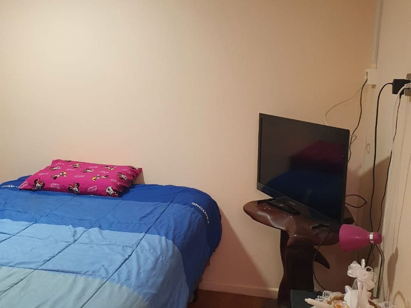 Dormitorio con cama de dos plazas, cojín rosado y un mueble con televisor en la esquina.