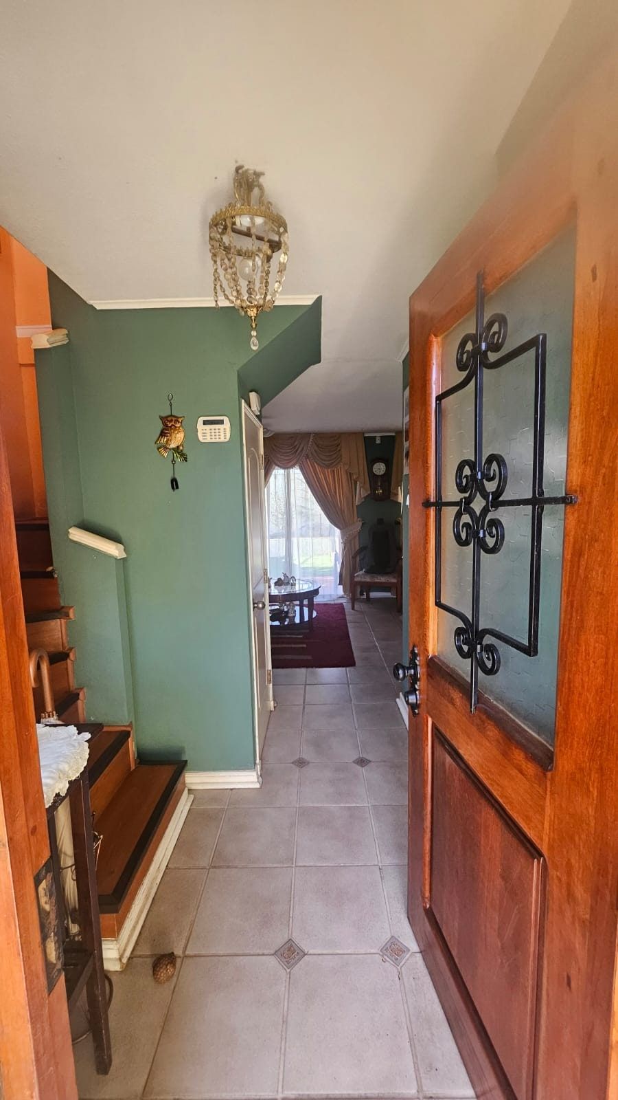 Pasillo de entrada con puerta de madera tallada, piso cerámico y teclado de alarma en el muro.