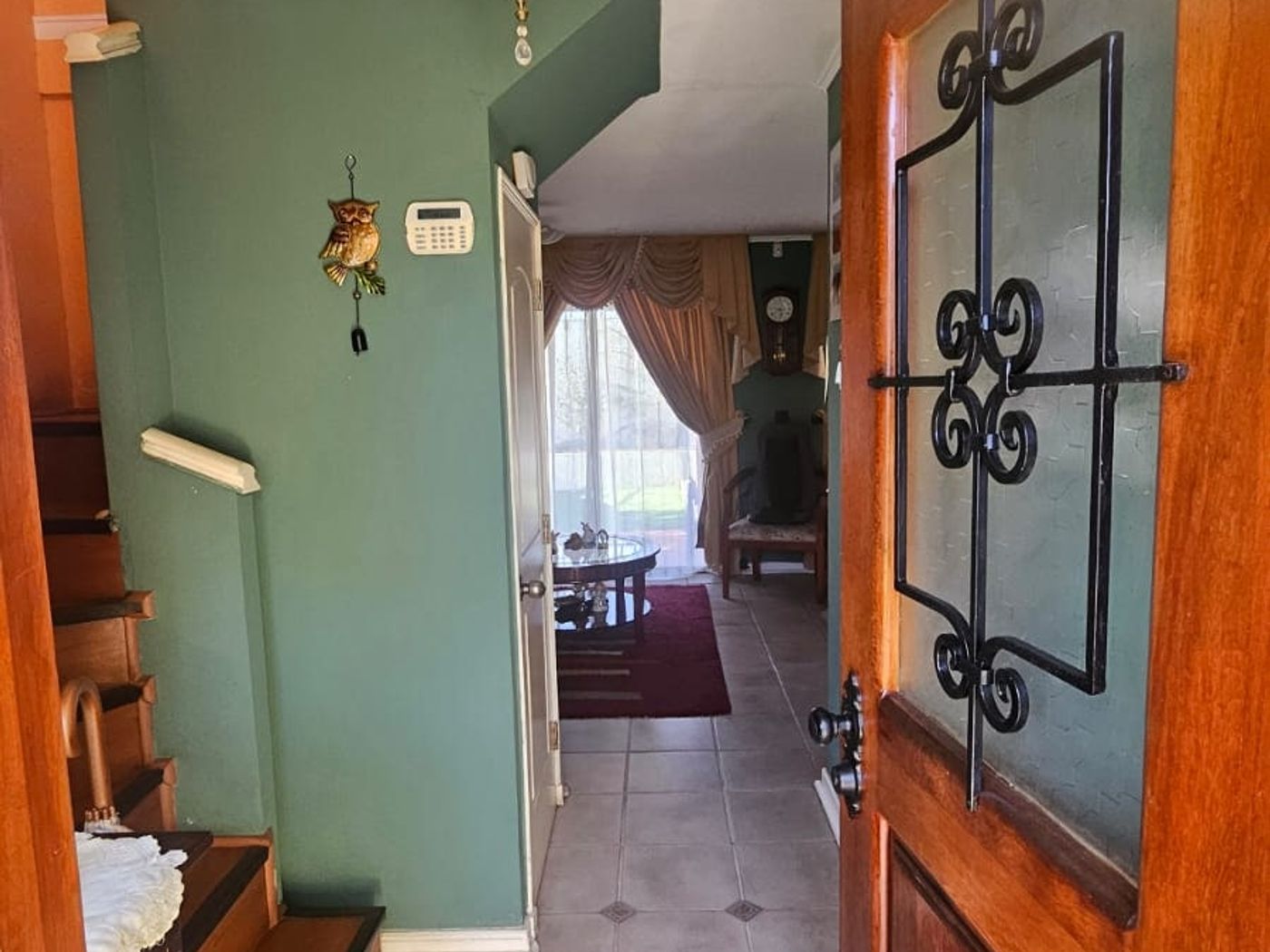 Pasillo de entrada con puerta de madera tallada, piso cerámico y teclado de alarma en el muro.
