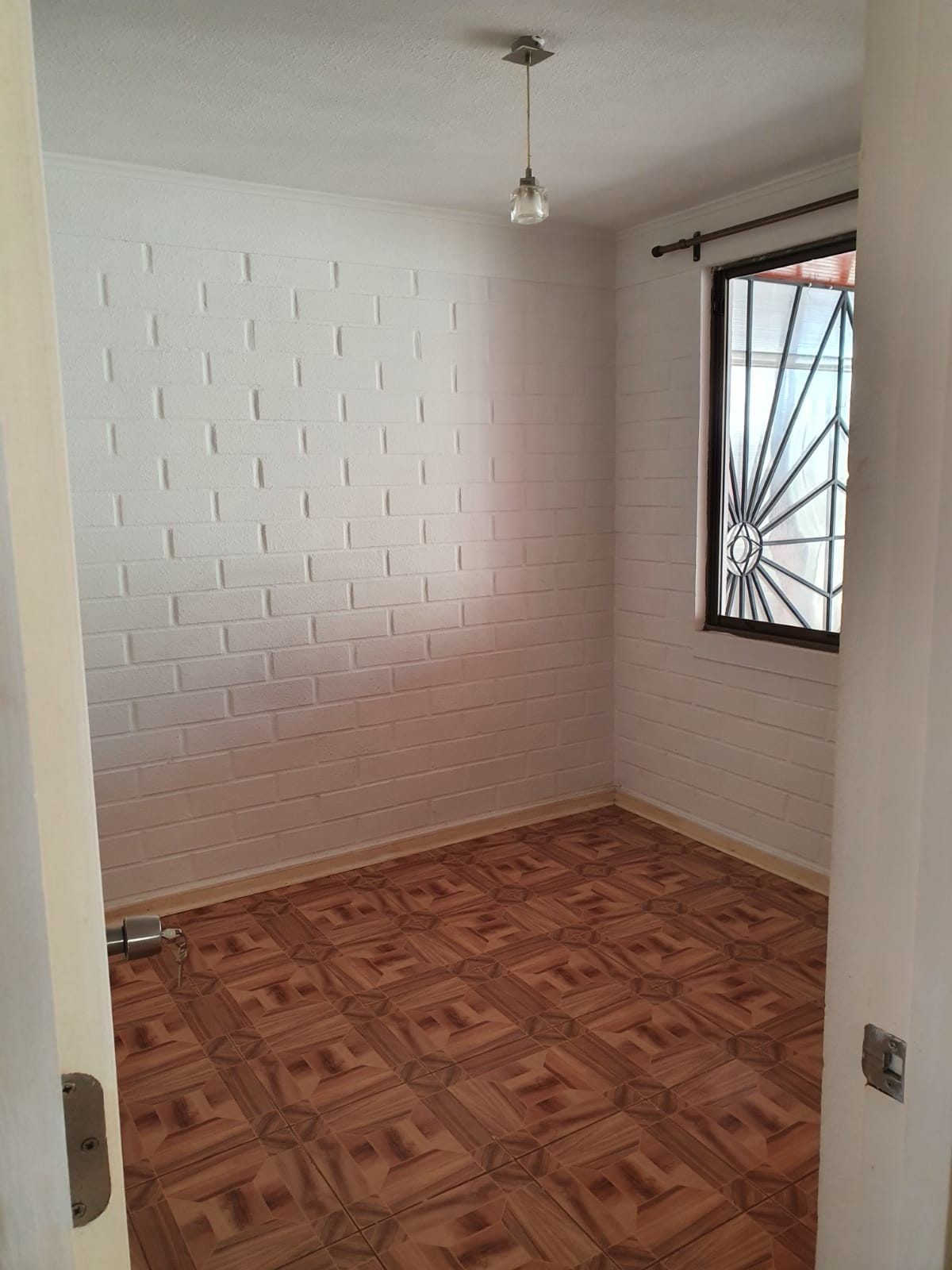 Dormitorio de planta baja con muros de ladrillo blanco, ventana esquinera y piso parquet cerámico.