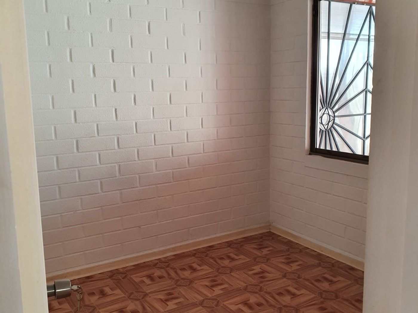 Dormitorio de planta baja con muros de ladrillo blanco, ventana esquinera y piso parquet cerámico.