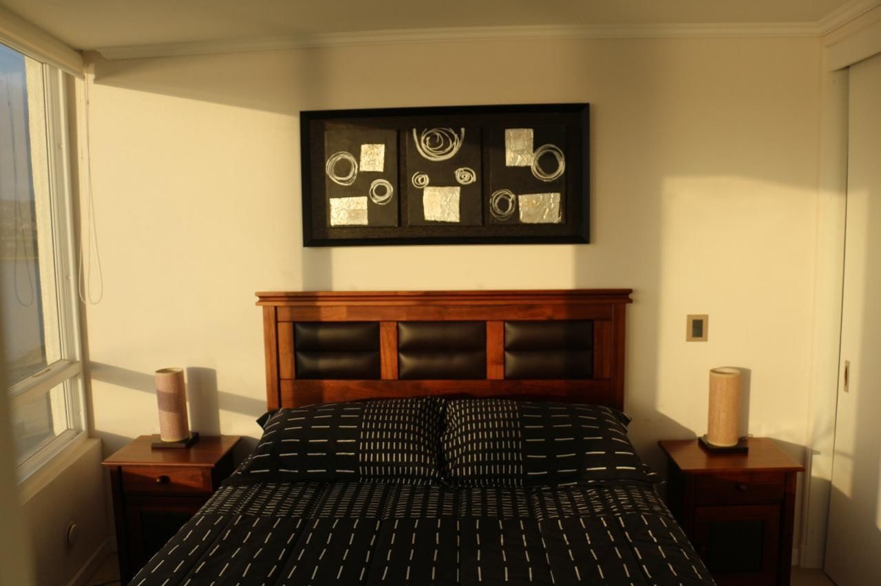Dormitorio principal con respaldo de madera, mesas de noche y cuadros decorativos abstractos.