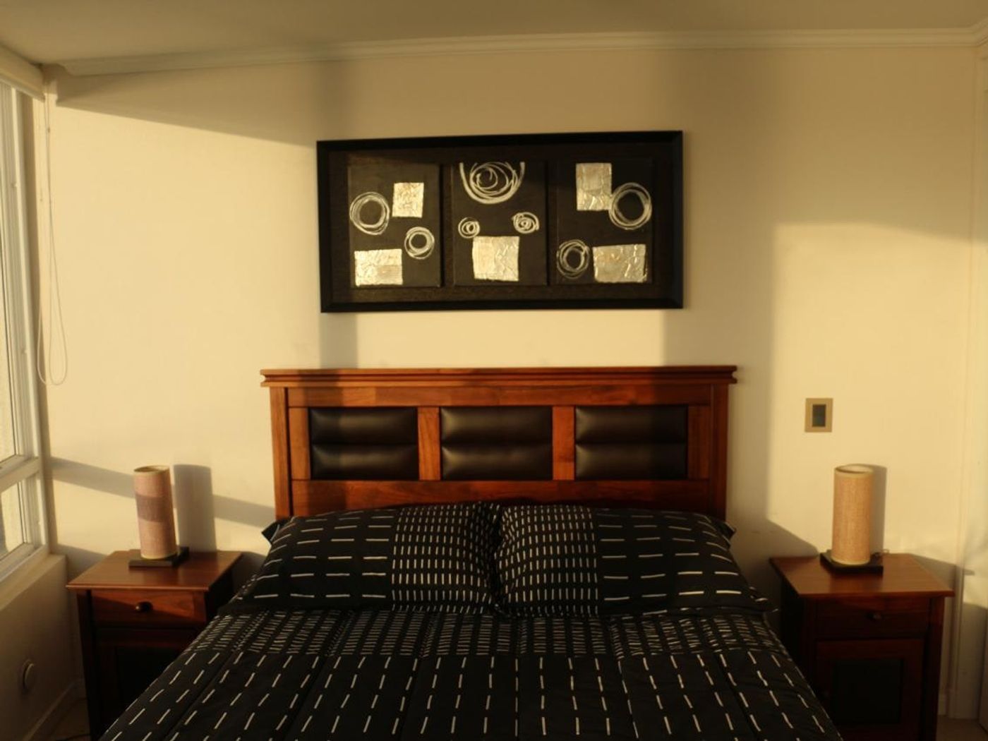 Dormitorio principal con respaldo de madera, mesas de noche y cuadros decorativos abstractos.