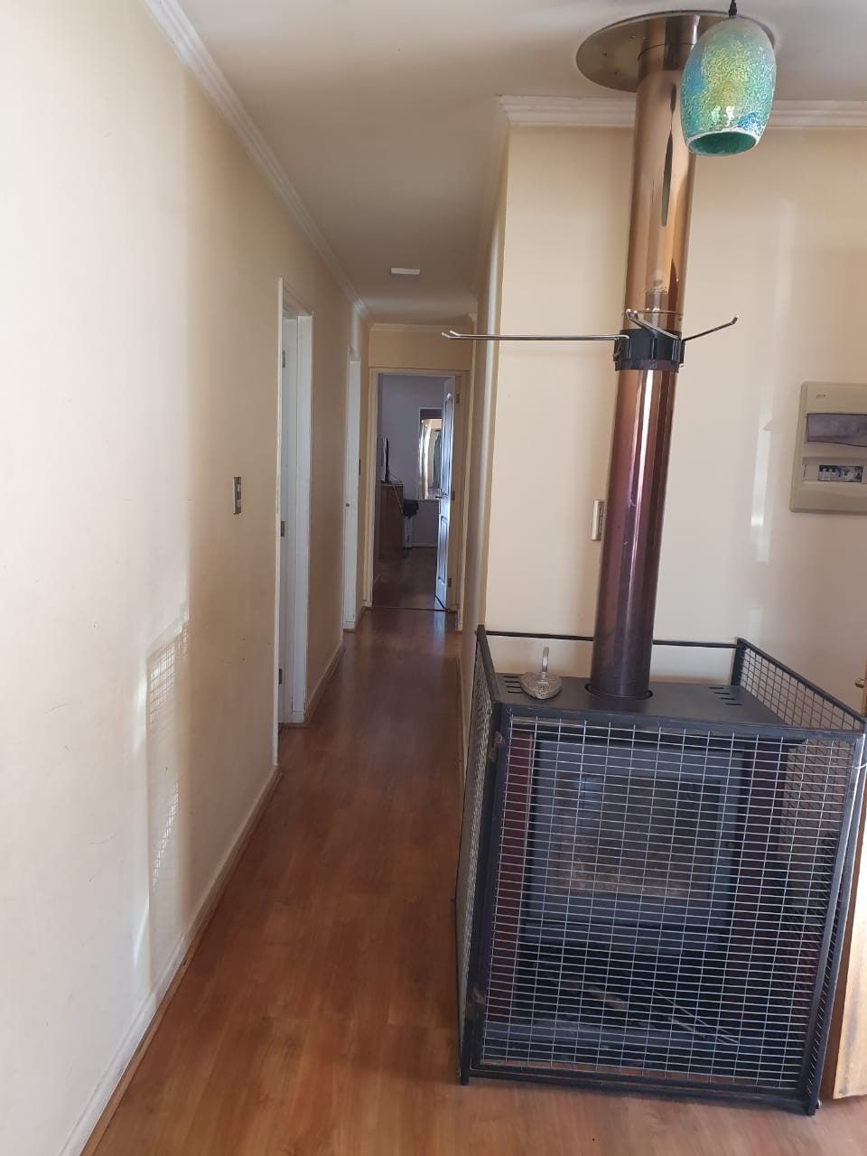 Pasillo interior con piso de madera, estufa a leña con protector de rejilla y acceso a dormitorios.