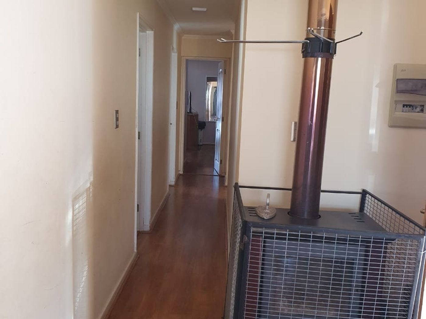 Pasillo interior con piso de madera, estufa a leña con protector de rejilla y acceso a dormitorios.