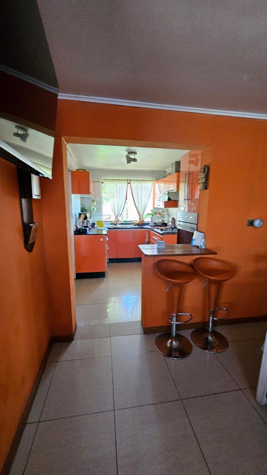 Barra con dos taburetes junto al acceso a la cocina naranja, paredes del mismo color.