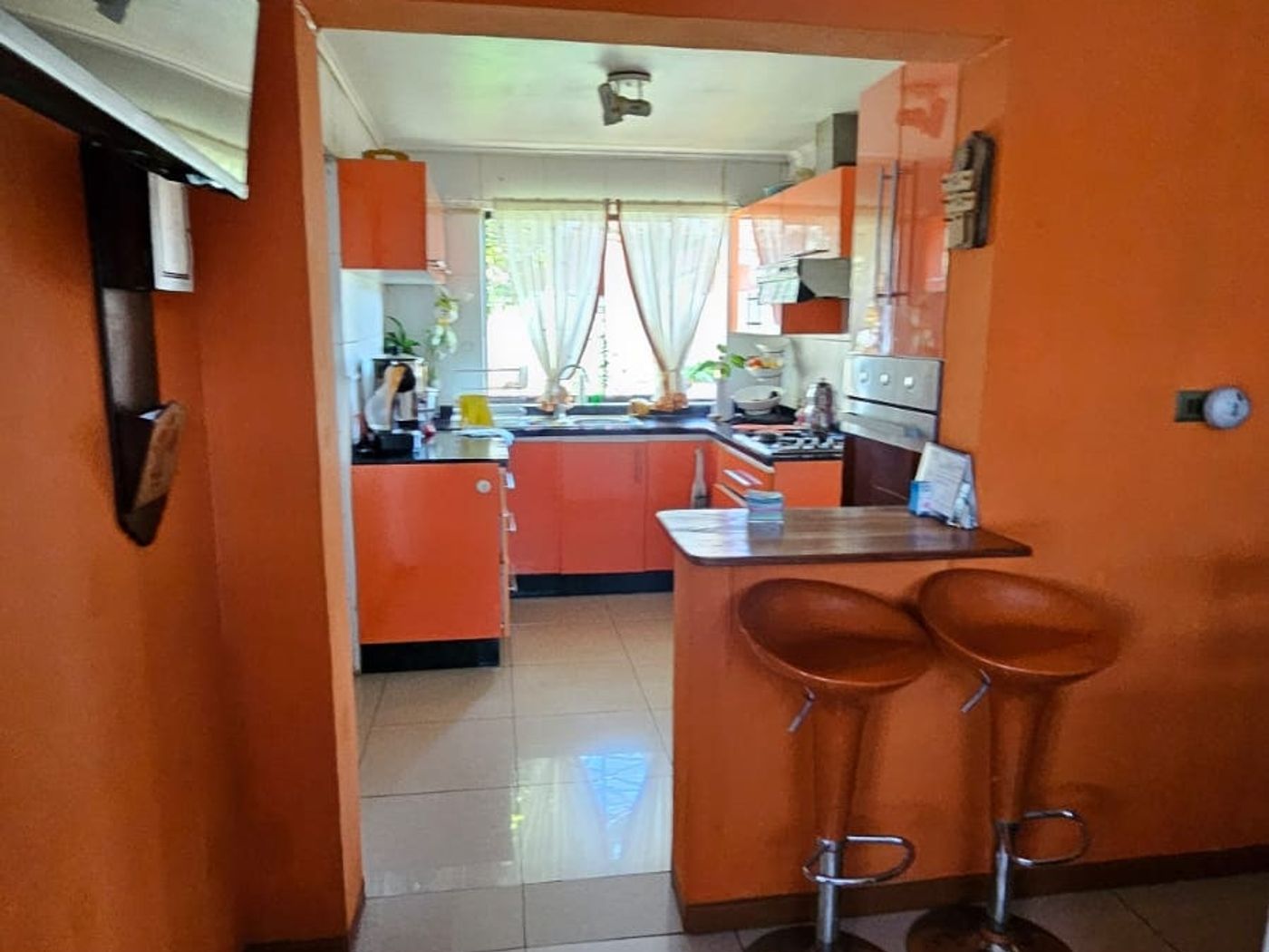 Barra con dos taburetes junto al acceso a la cocina naranja, paredes del mismo color.