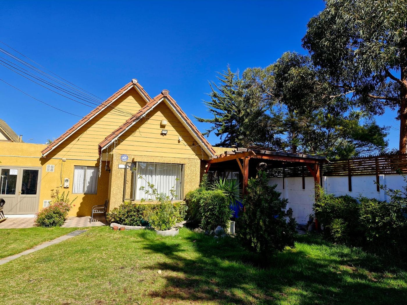 Fachada de casa color amarillo con techo a dos aguas de tejas rojas y jardín delantero.