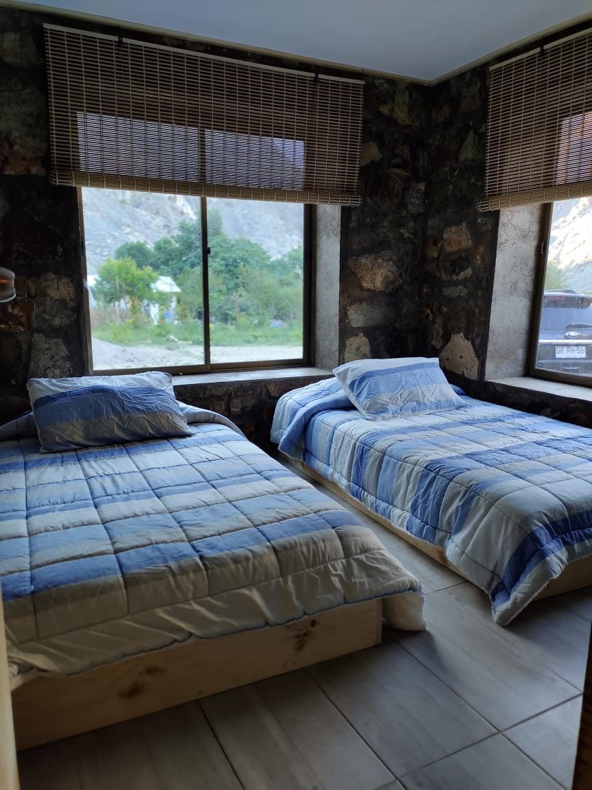 Dormitorio con dos camas, muros de piedra y ventanas amplias