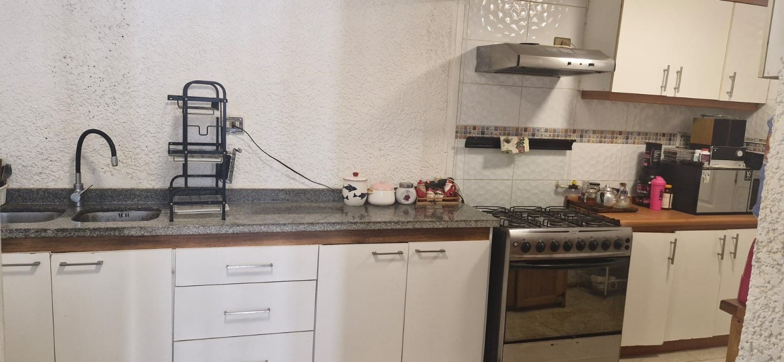 Cocina con muebles blancos, cocina a gas de cuatro platos, campana extractora y cubierta de granito.