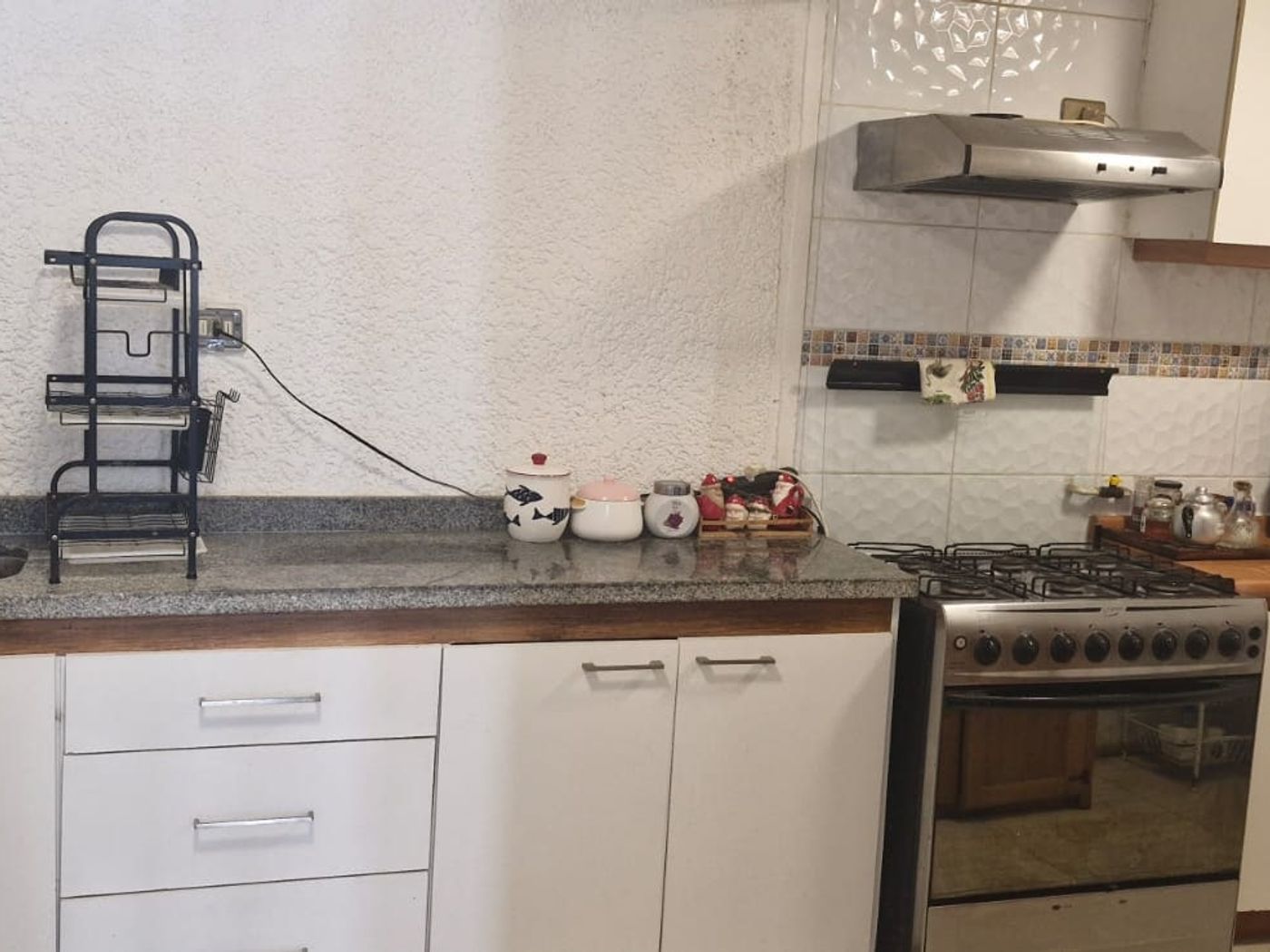 Cocina con muebles blancos, cocina a gas de cuatro platos, campana extractora y cubierta de granito.
