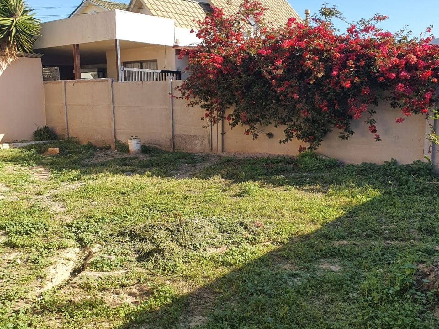 Vista de la casa desde el patio, con techos a dos aguas, terraza cubierta y buganvilia junto al muro.