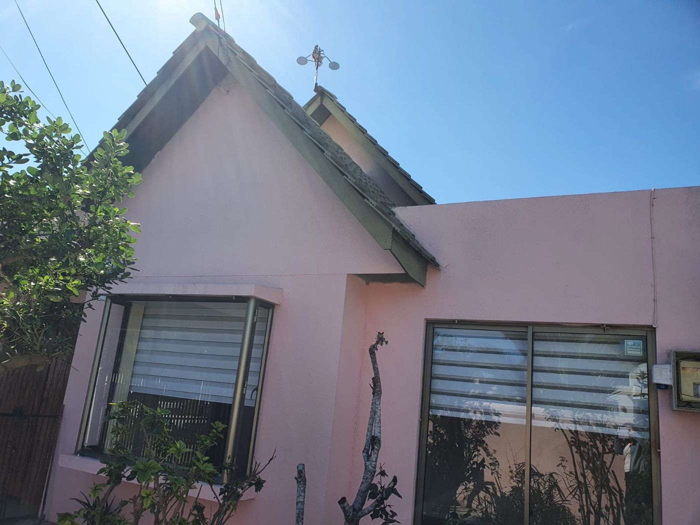 Fachada frontal de la casa con muros color rosado, techumbre a dos aguas y antejardín.