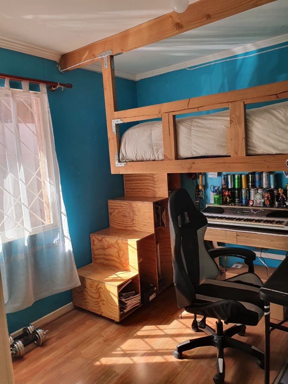 Vista general del dormitorio con cama en altillo, escalera de madera y escritorio al fondo.