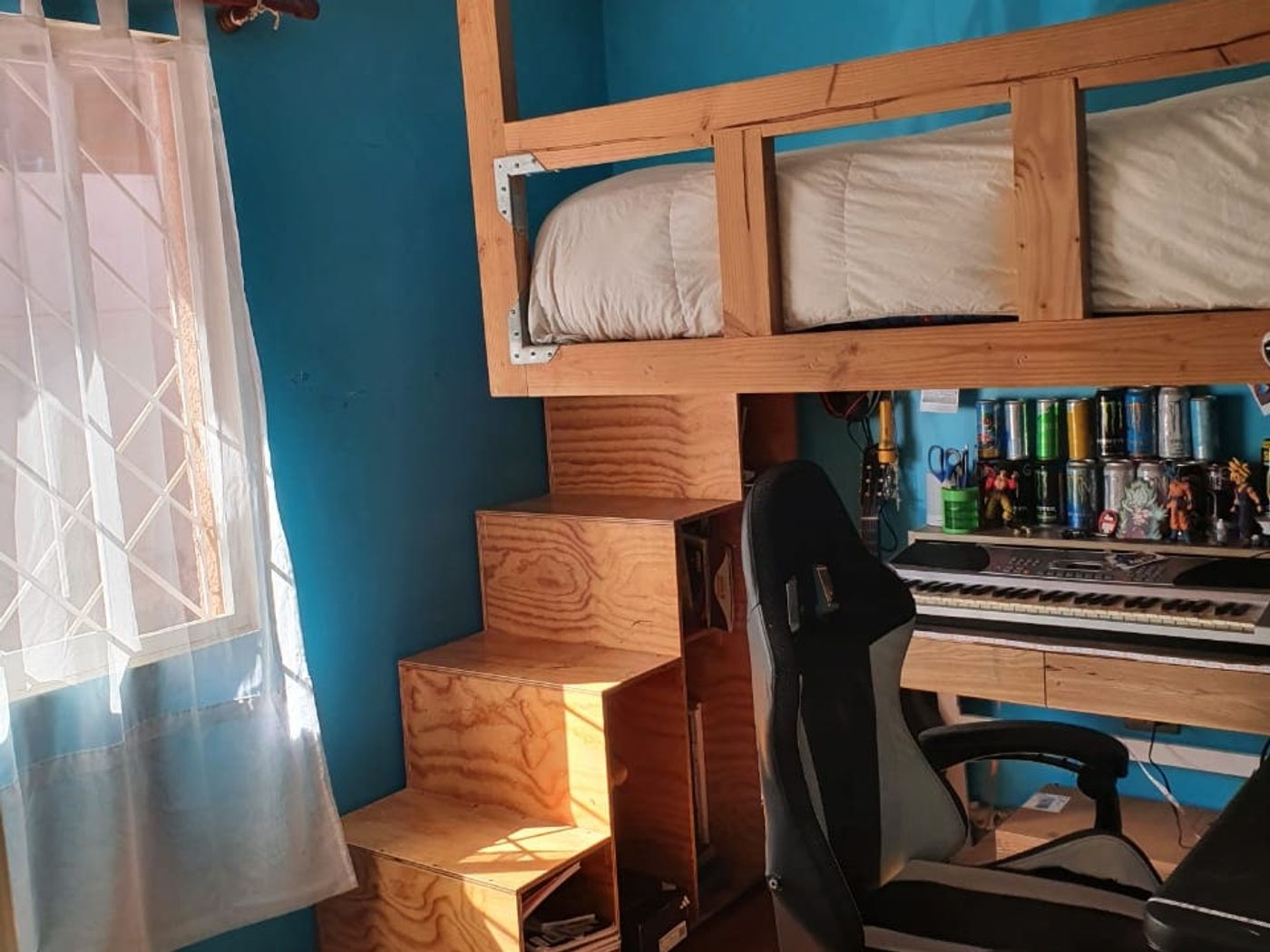 Vista general del dormitorio con cama en altillo, escalera de madera y escritorio al fondo.