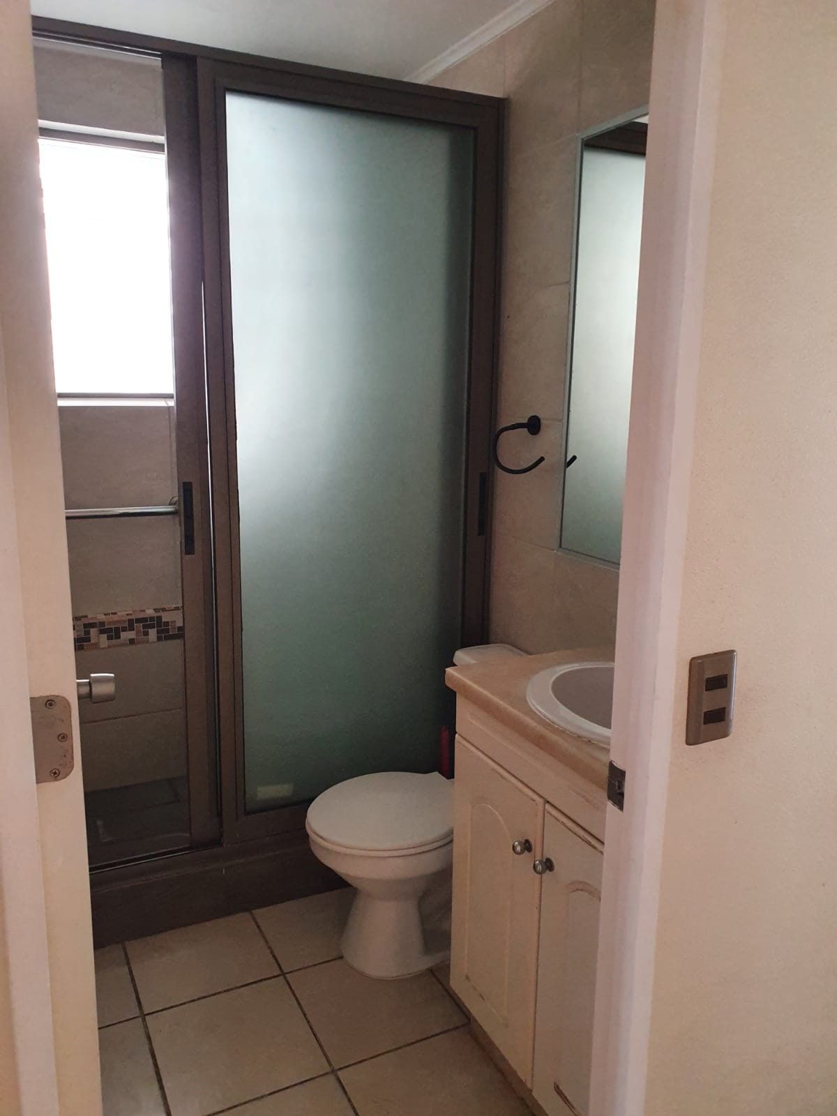 Baño con vanitorio, inodoro, espejo mural y ducha con mampara corrediza de vidrio esmerilado.