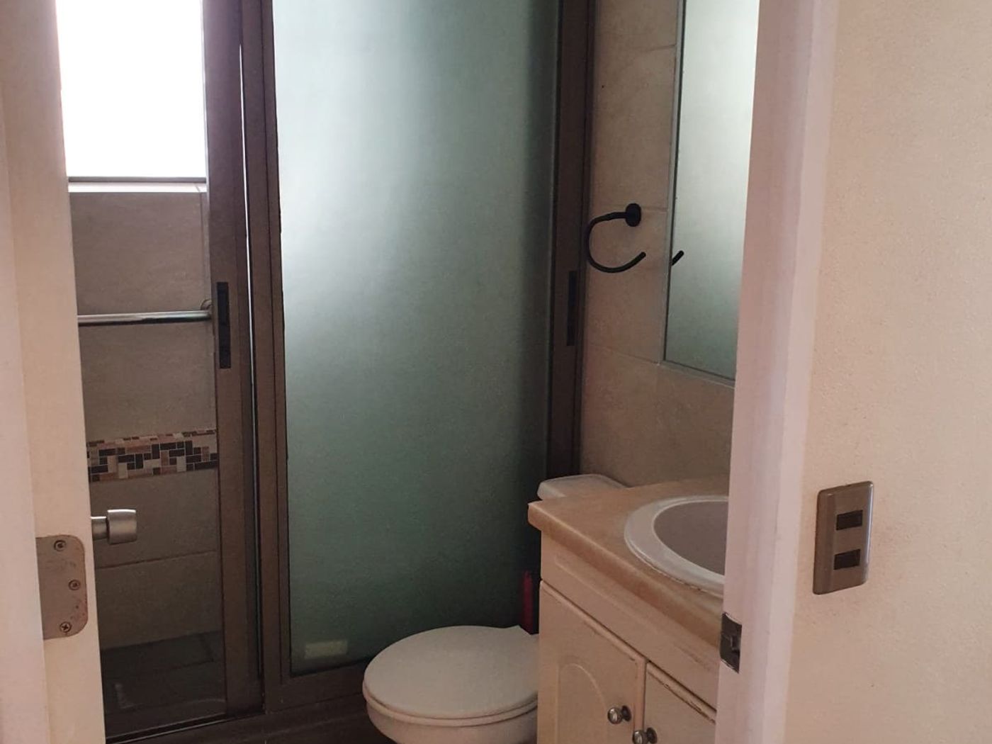 Baño con vanitorio, inodoro, espejo mural y ducha con mampara corrediza de vidrio esmerilado.