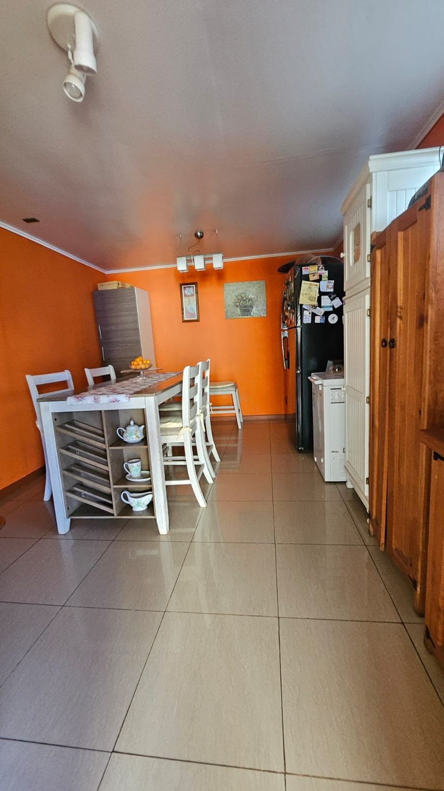 Comedor junto a la cocina con mesa blanca, sillas y refrigerador negro sobre pared naranja.