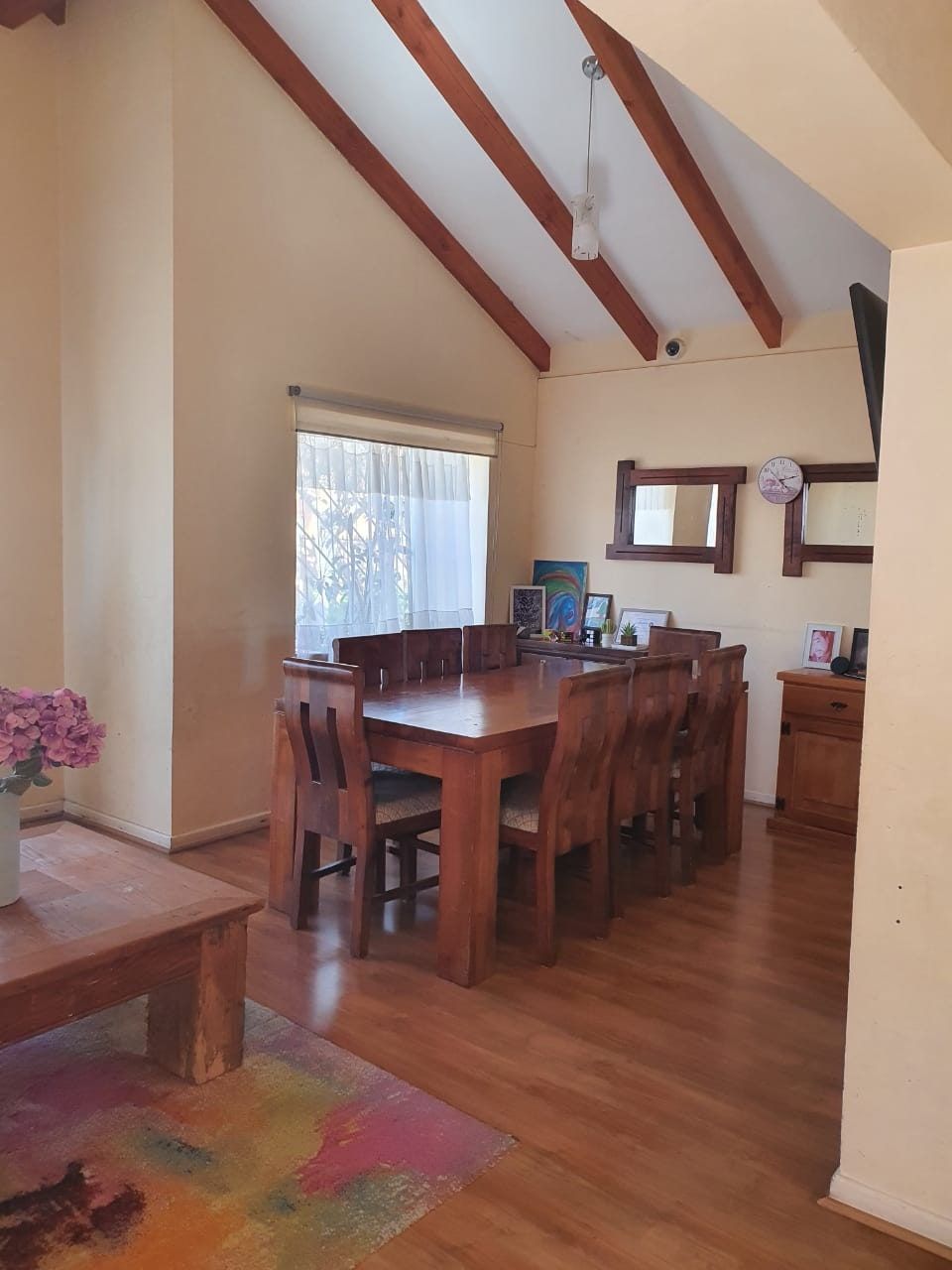 Comedor con mesa para ocho sillas, espejos en la pared y repisa con fotos enmarcadas pequeñas al fondo.