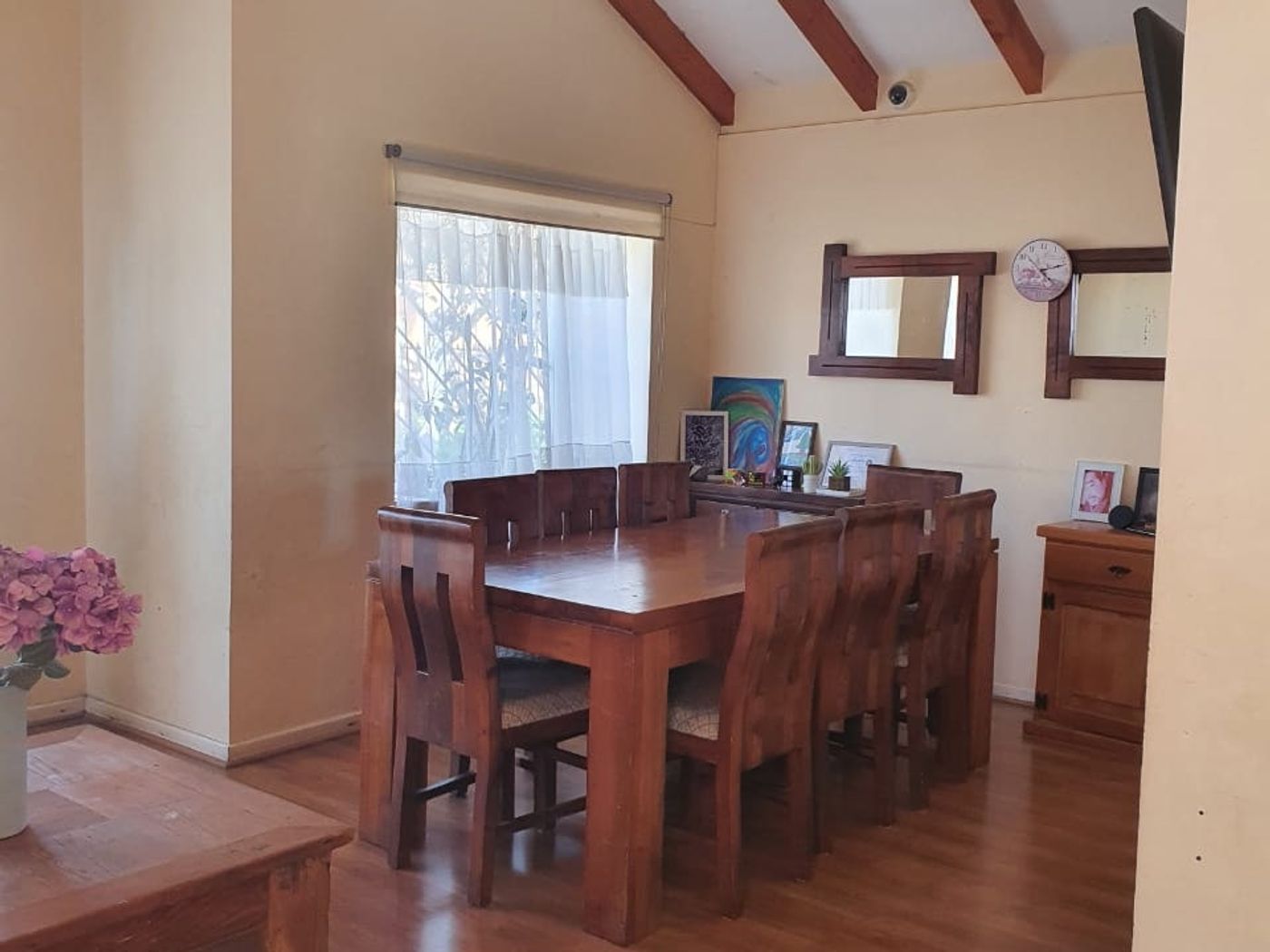 Comedor con mesa para ocho sillas, espejos en la pared y repisa con fotos enmarcadas pequeñas al fondo.