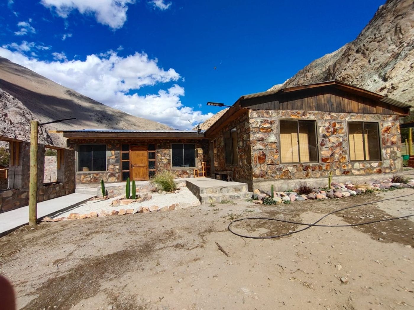 Frente de la casa de piedra con cerros y cielo despejado