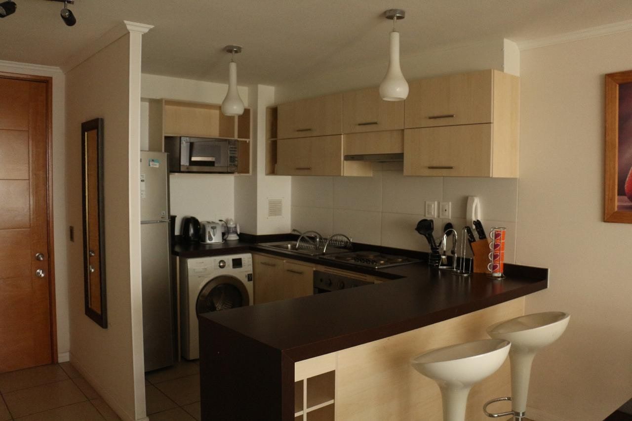 Cocina equipada con encimera eléctrica, horno empotrado, campana, lavadora y muebles aéreos.
