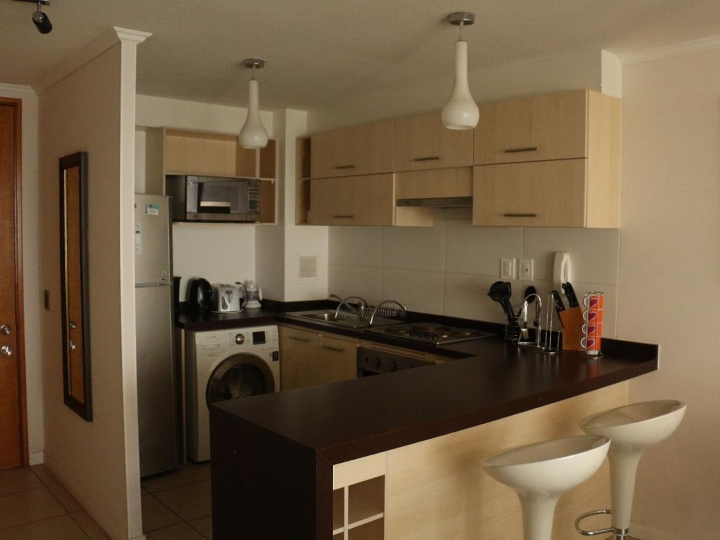 Cocina equipada con encimera eléctrica, horno empotrado, campana, lavadora y muebles aéreos.
