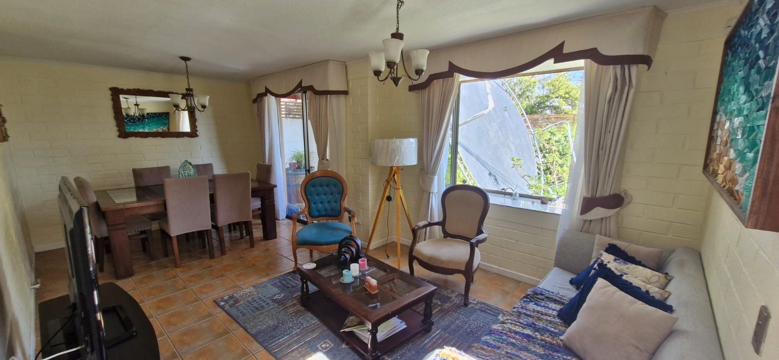 Living comedor con mesa de madera, sillón tapizado, sofá, alfombra y ventana con vista al jardín.