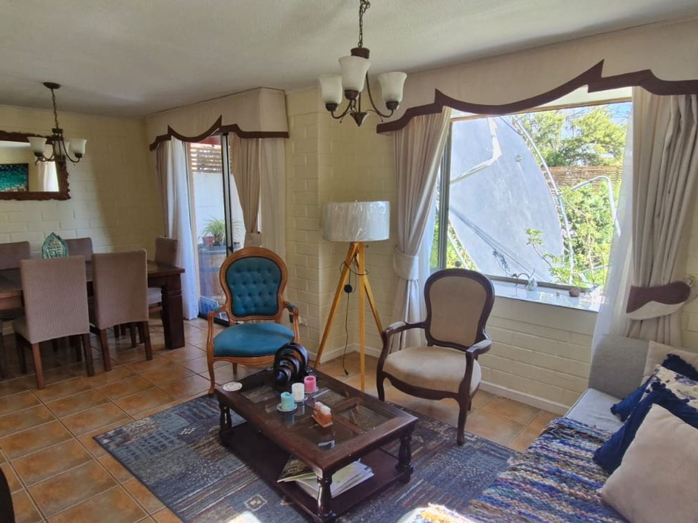 Living comedor con mesa de madera, sillón tapizado, sofá, alfombra y ventana con vista al jardín.