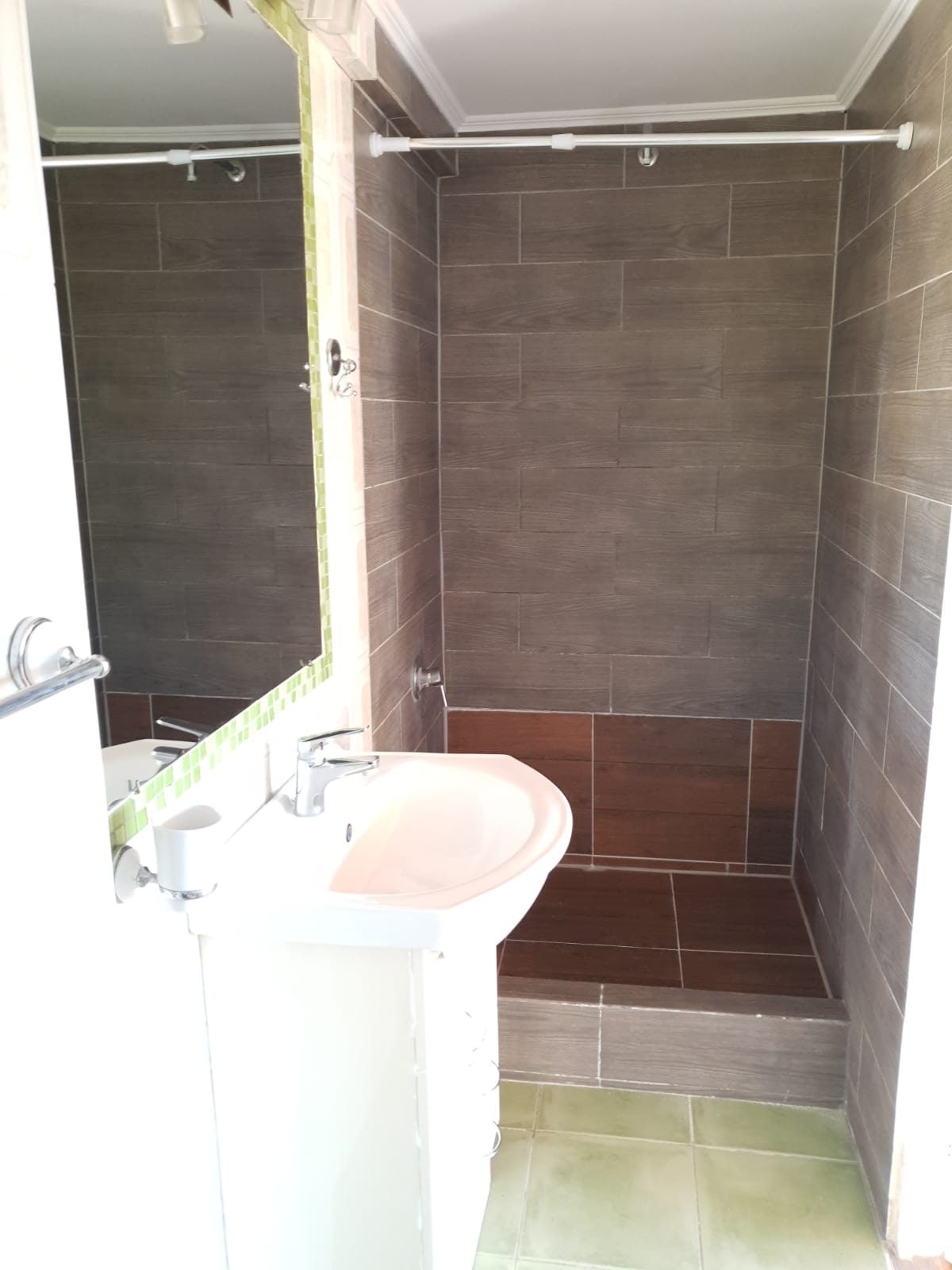 Baño completo revestido en cerámica gris tipo piedra con lavamanos de pedestal y ducha.