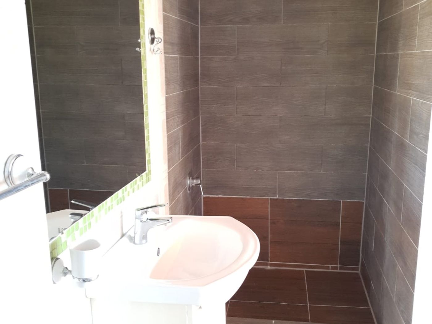 Baño completo revestido en cerámica gris tipo piedra con lavamanos de pedestal y ducha.