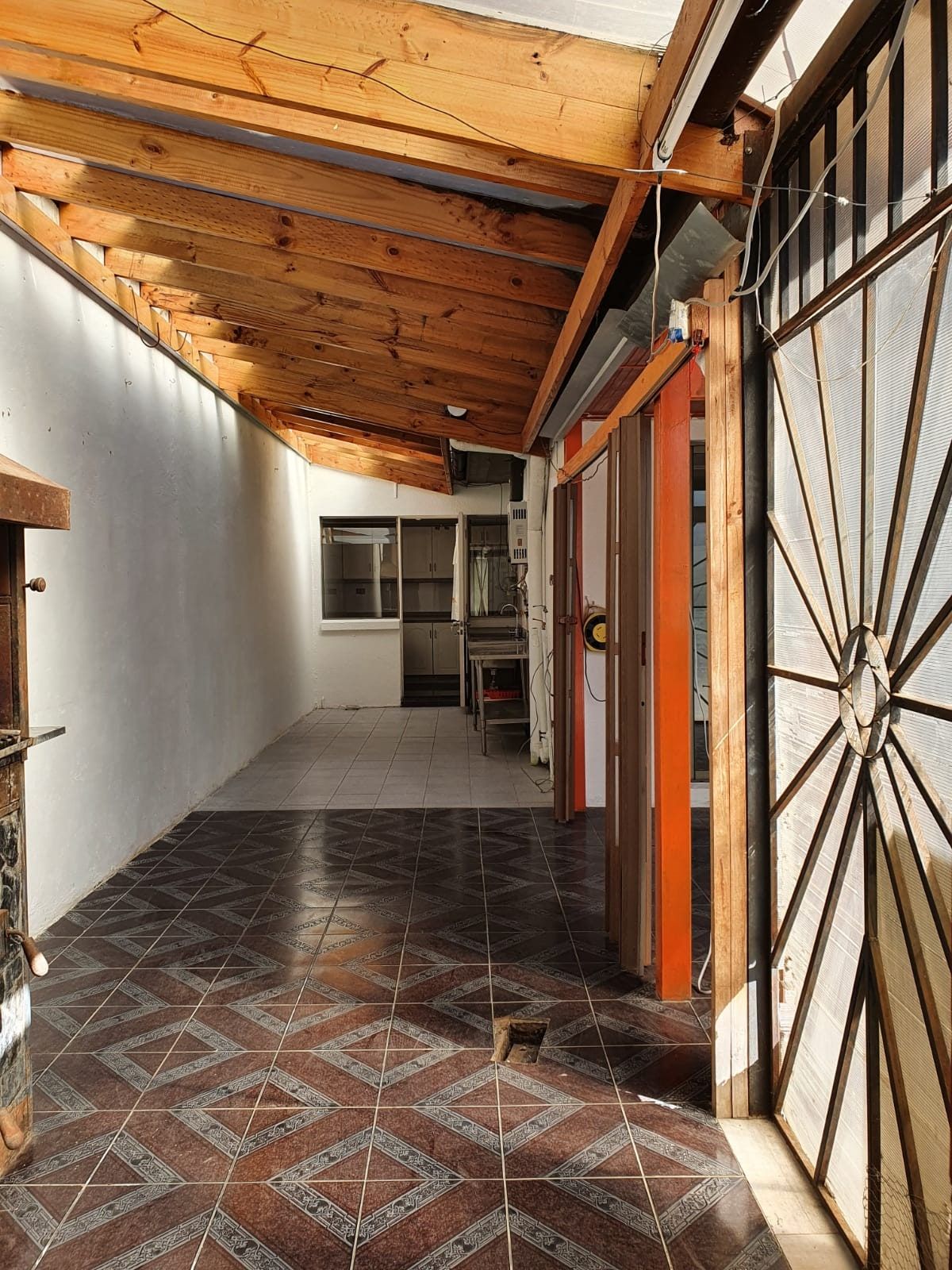 Galería lateral techada con entramado de pérgola de madera, piso cerámico y cierre perimetral.